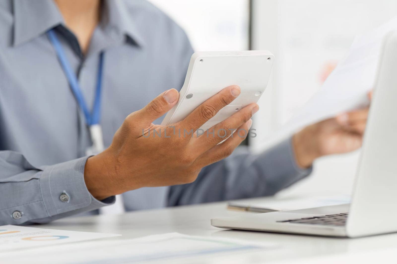 A professional in a remote work setting, using a calculator while holding documents, highlighting analytical skills and productivity.