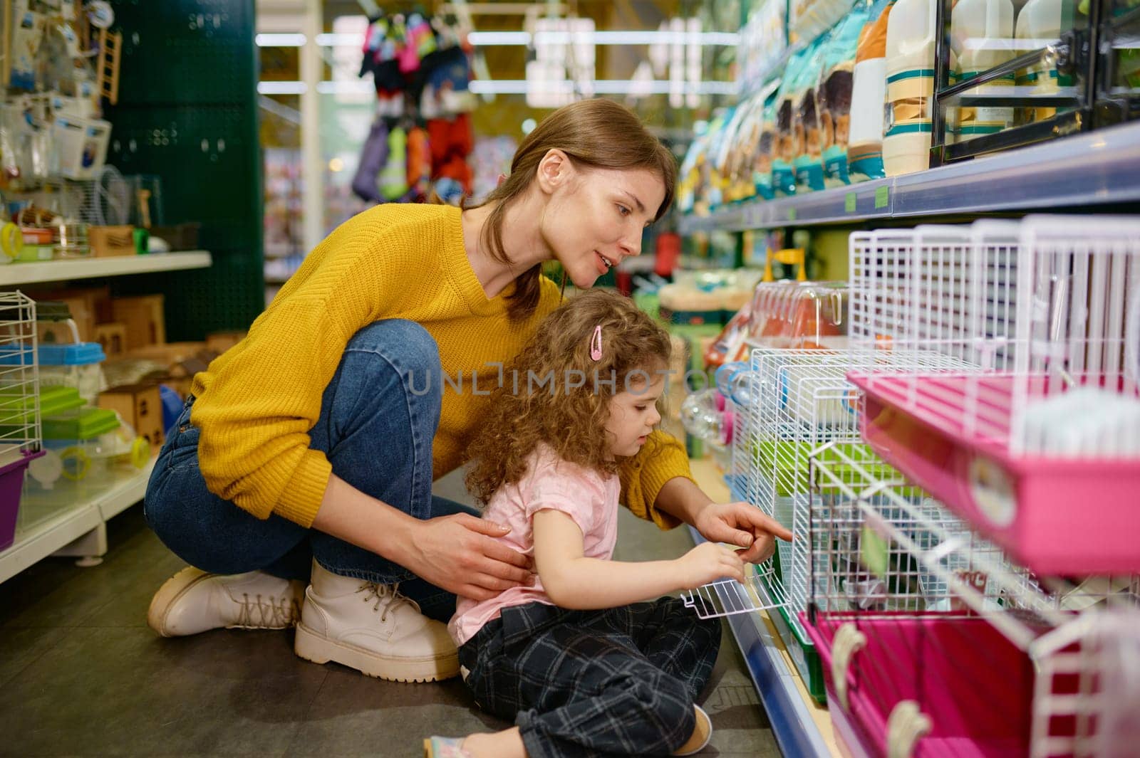 Smiling woman with her daughter choosing hamster or other rodent at pet shop. Happy family enjoying purchase new pet
