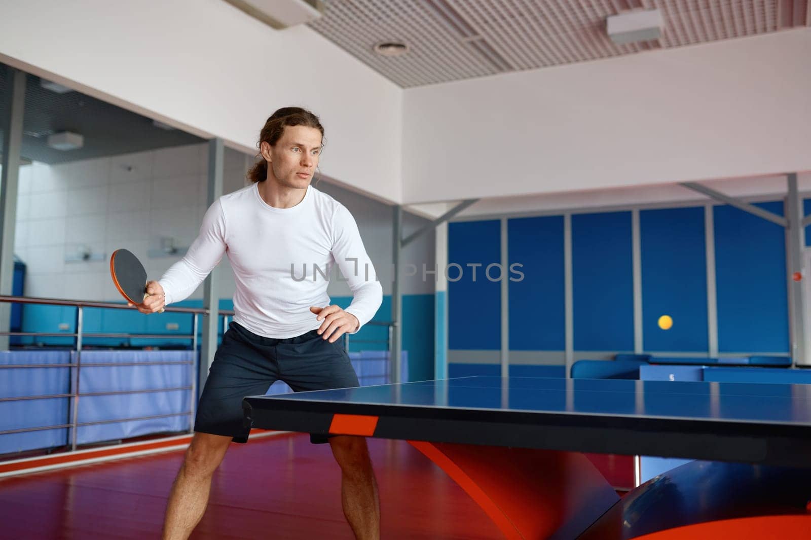 Portrait of young table tennis player training in sport club. Hipster guy enjoying ping pong game practicing technique