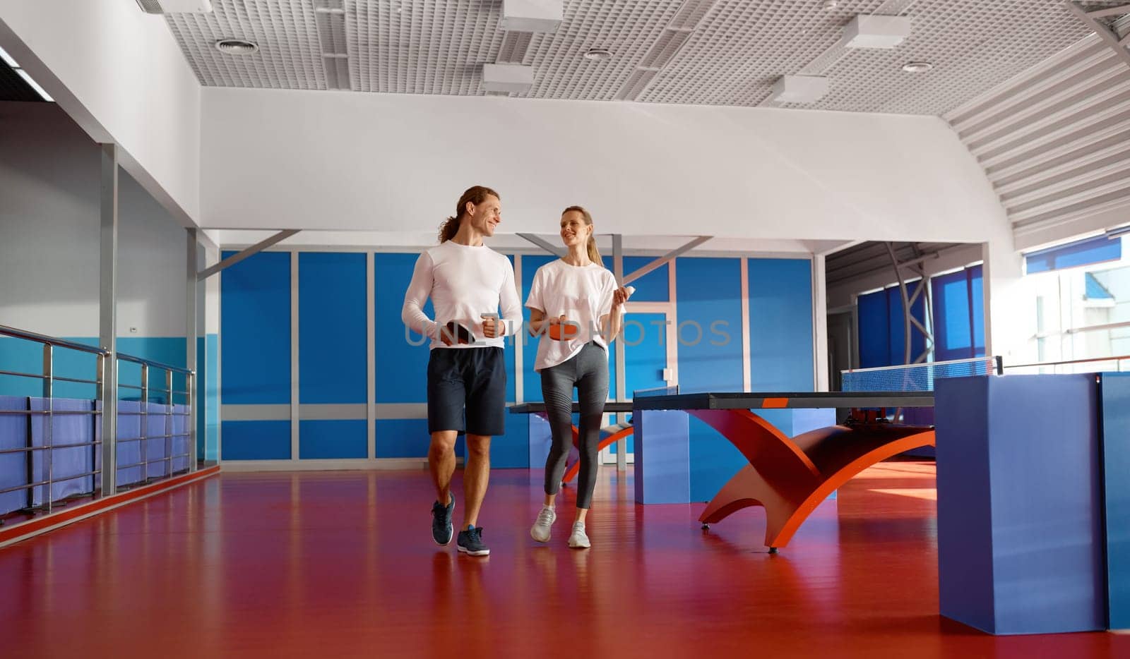 Male and female friends walking and talking after training class at ping pong sport club. Two table tennis player sharing emotions