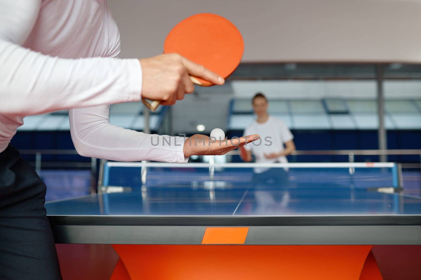 Man and woman playing table tennis, focus on sportsman player serving ball with racket. Sport and healthy lifestyle concept. Closeup view
