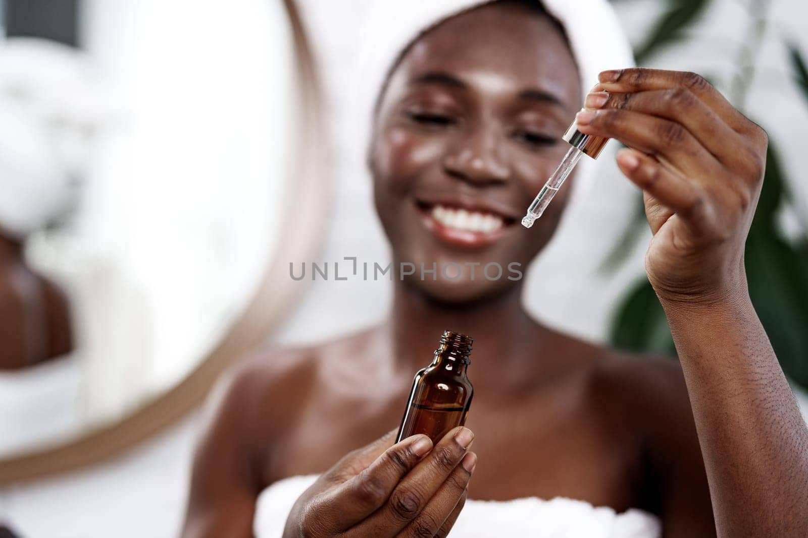 A woman enjoys her skincare routine at home, holding a dropper bottle filled with serum. She smiles brightly while applying the serum, surrounded by a serene atmosphere.