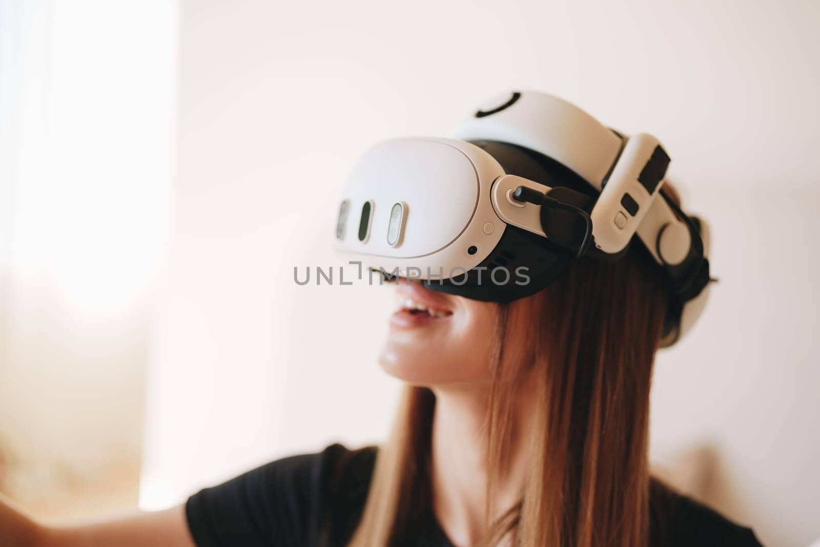 A young woman fully engaged in a virtual reality experience is wearing a sleek VR headset. She appears focused, enjoying the immersive technology in a modern and bright room.