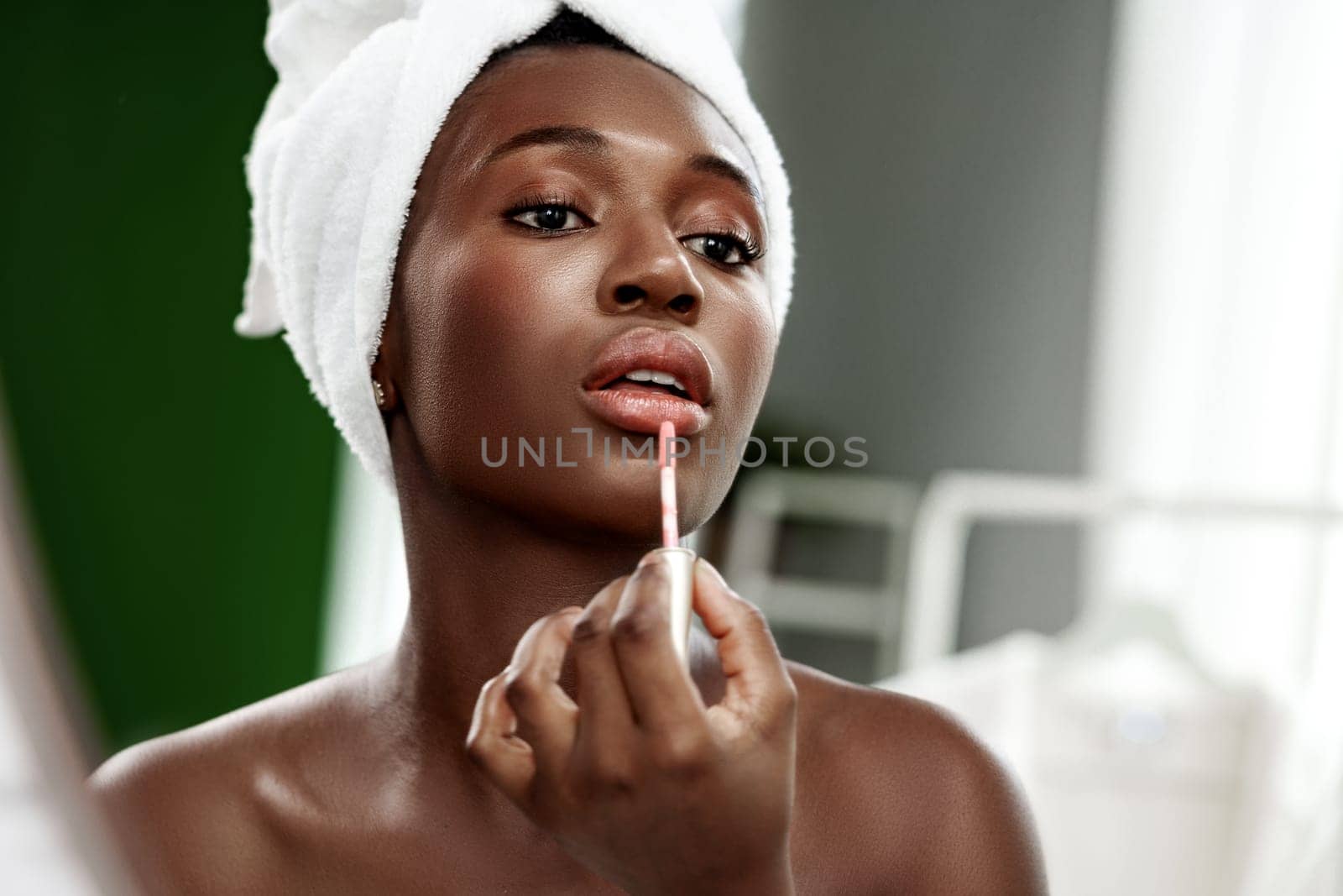 A woman focuses on applying lip gloss in a stylish, well-lit environment. The calming atmosphere highlights her beauty routine in a cozy home setting.