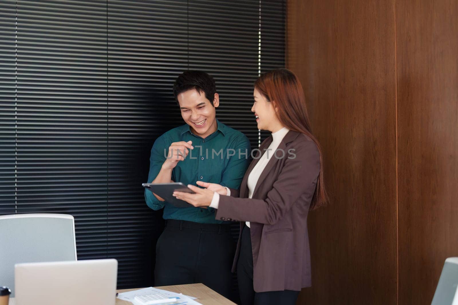 Two professionals in an office environment engage in a productive discussion over a tablet, highlighting the power of teamwork and innovation.