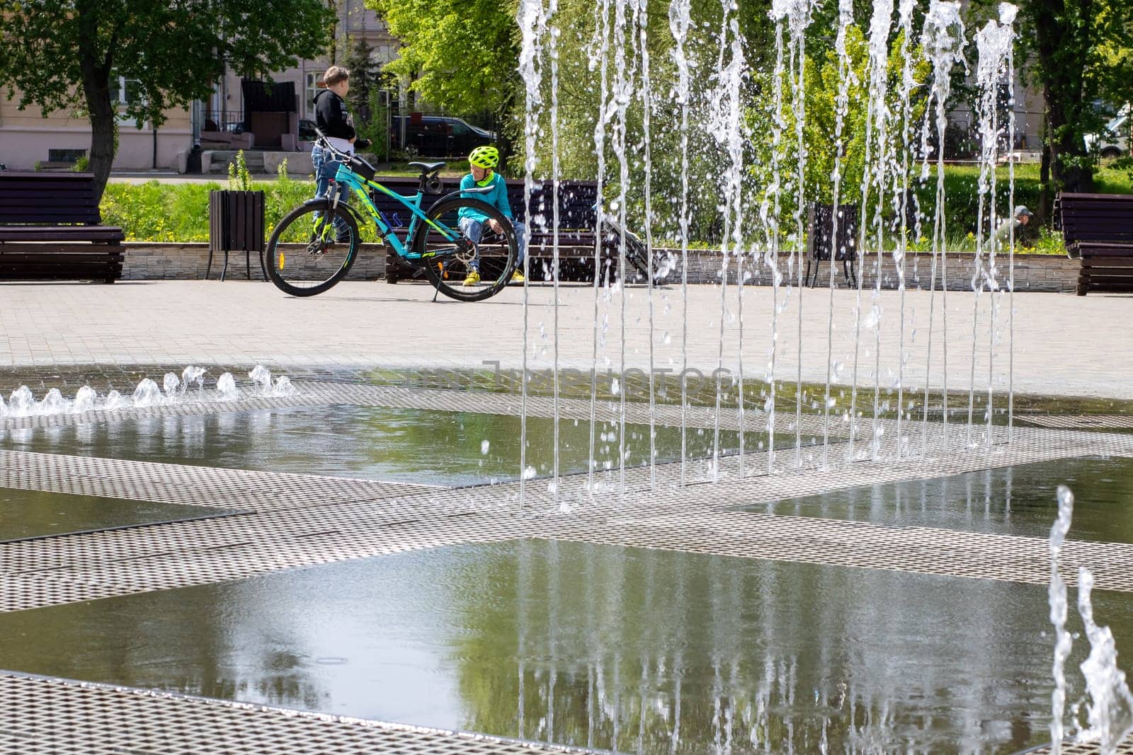 A person skillfully riding a bicycle in front of a beautifully designed fountain, enjoying the refreshing sight and sound of water splashing all around