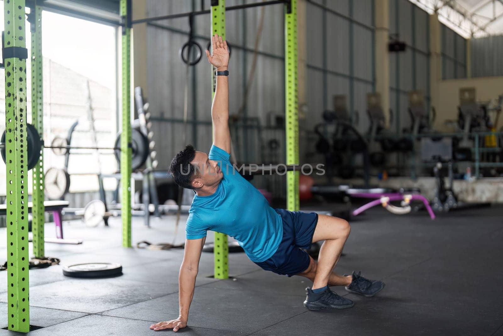 A man performs a side plank variation, emphasizing balance and core strength in a modern gym environment.