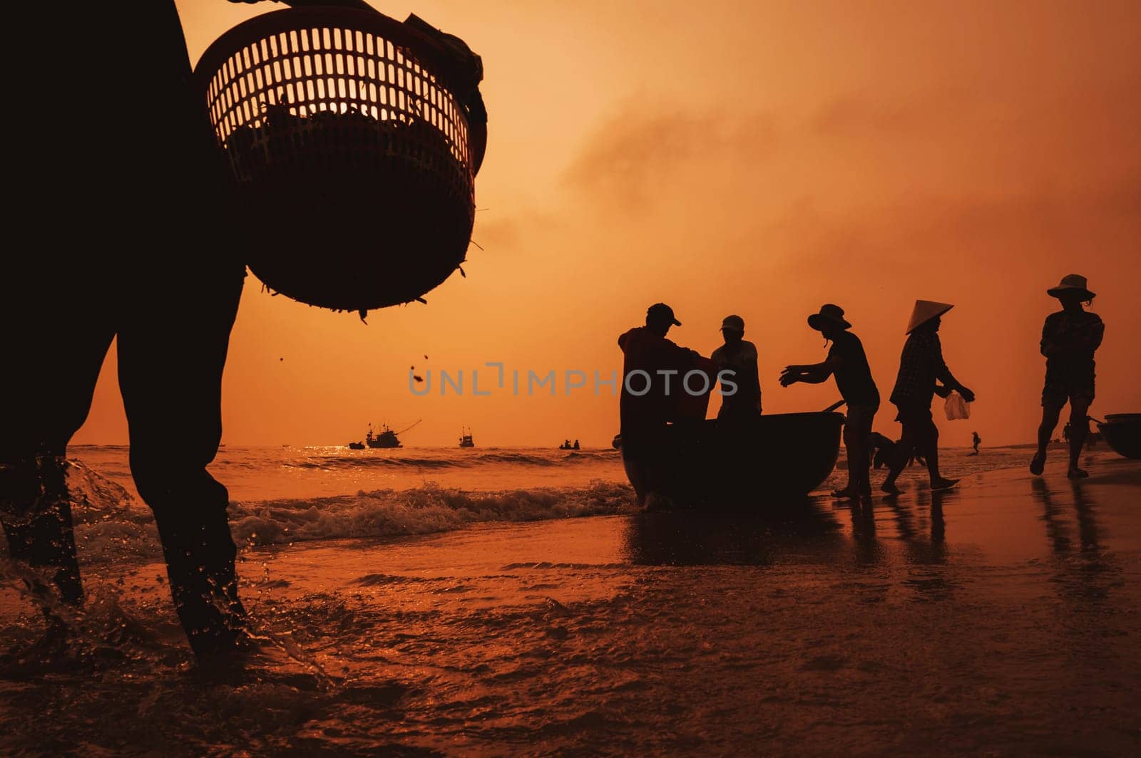 Silhouettes of Vietnamese fishermen and women on coast by sea at fish market Tam Tien in fishing village in morning at dawn in Vietnam. Tam Tien, Quang Nam province, Vietnam - April 10, 2025