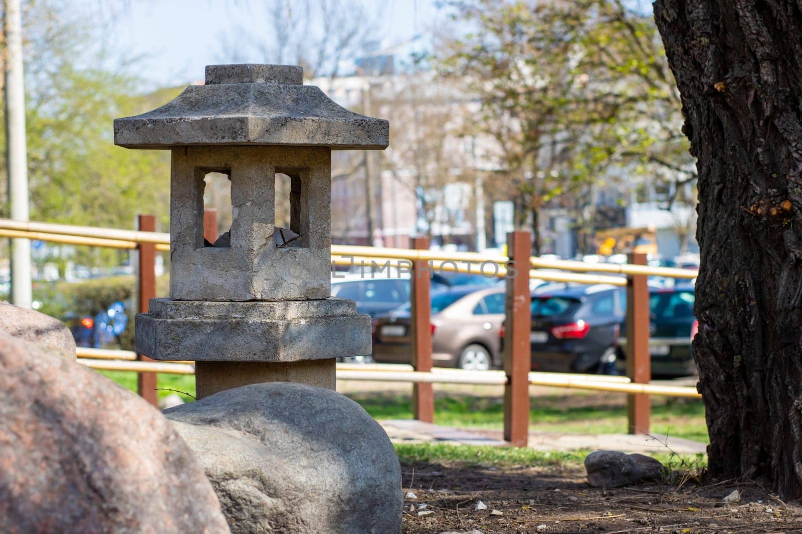 A beautifully crafted stone lantern is situated right next to a lush tree in a serene park, providing an inviting atmosphere
