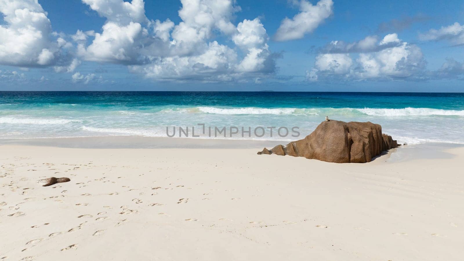 Rocky outcrop on a clear sandy beach with turquoise sea. La Digue, Seychelles. Petite Anse Beach.
