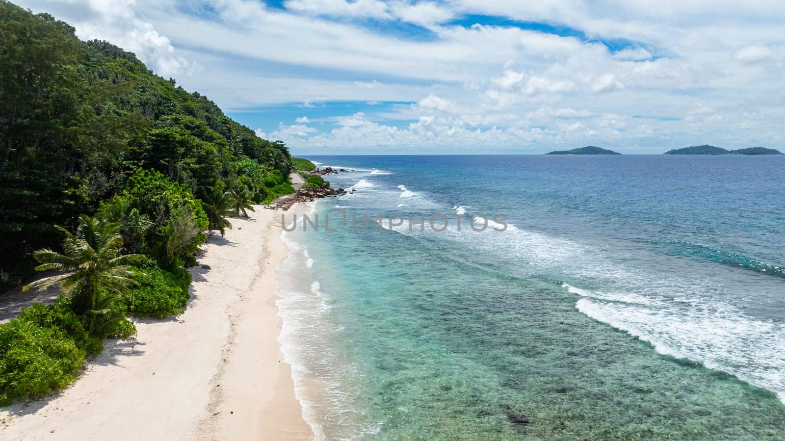 A beautiful white sandy beach with overhanging palm trees and crystal-clear waters stretching into the distance. Seychelles, La Digue.