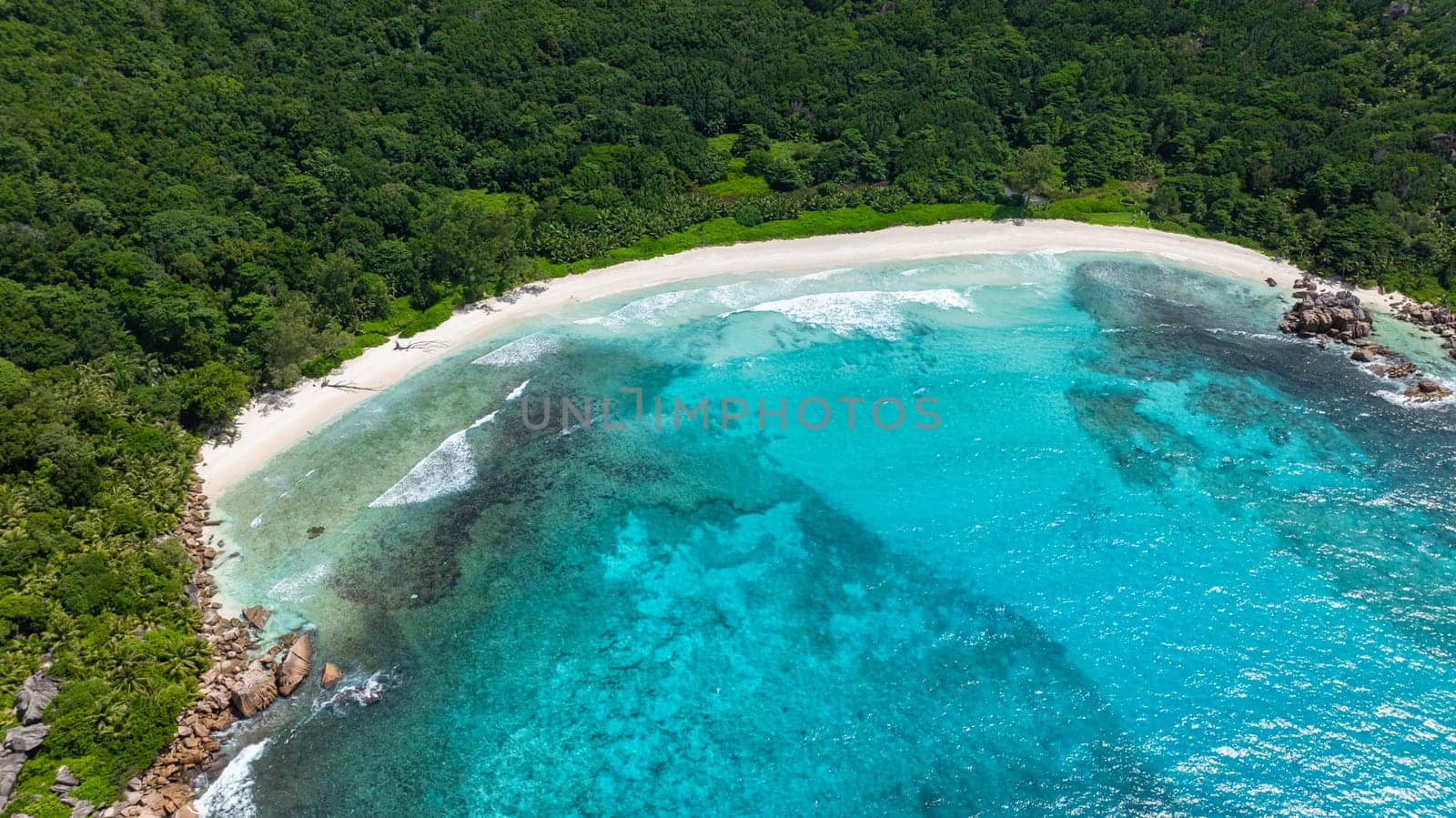 Lush island coastline surrounded by clear blue ocean waters and a rocky shore. Anse Cocos beach. La Digue, Seychelles.