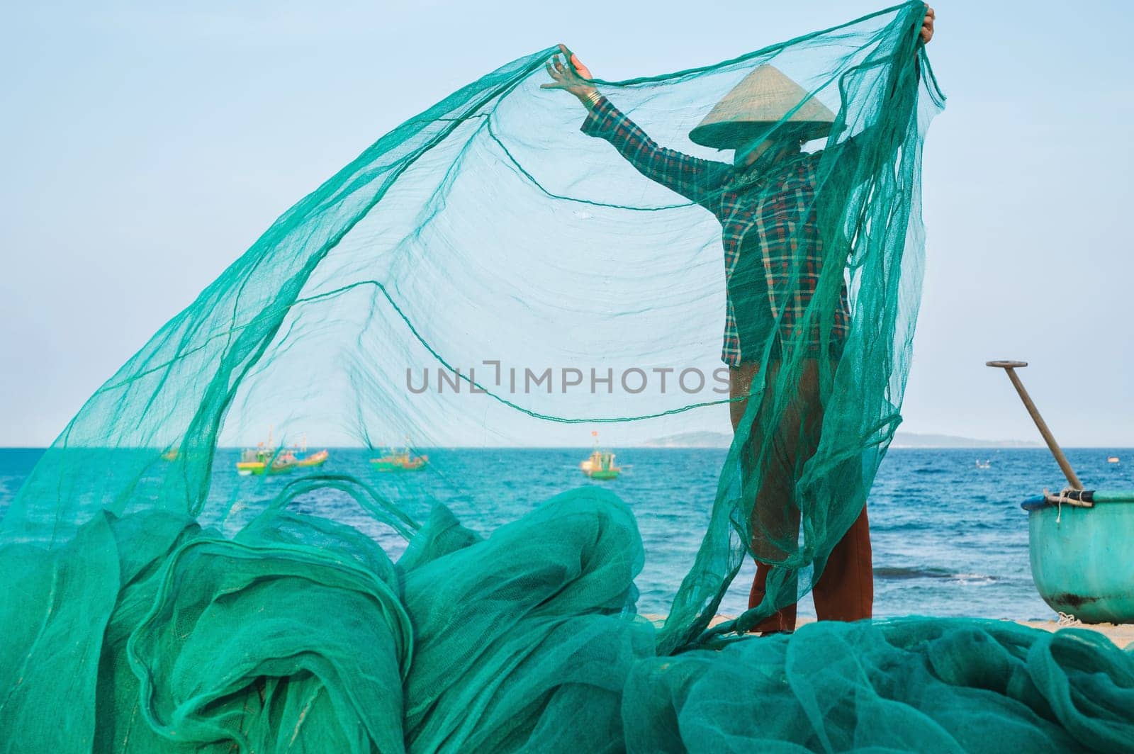Vietnamese woman in a traditional straw hat checks the catch of fish in a fishing net on beach by sea in a fishing village in Vietnam