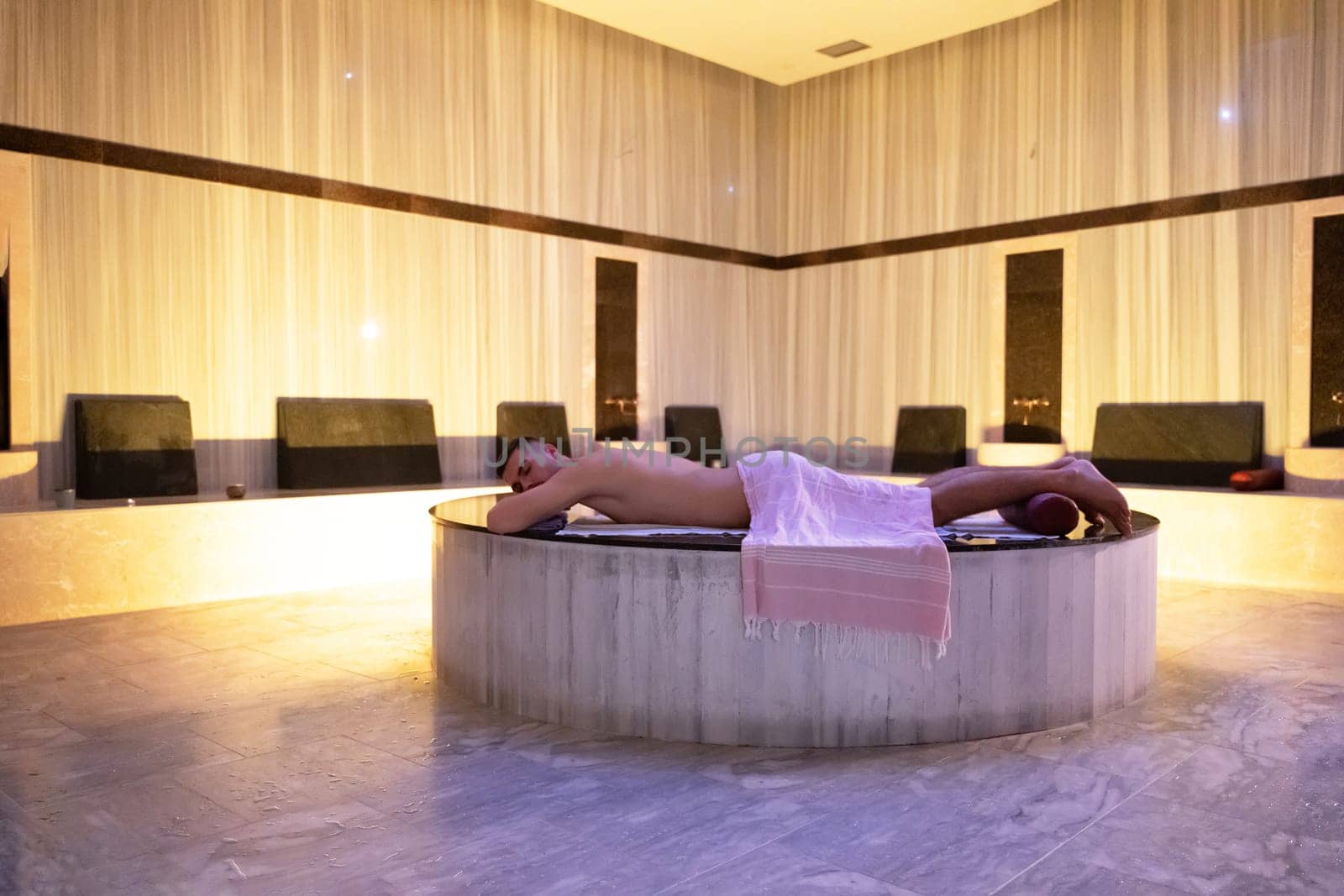 Turkish Bath Relaxation.Man relaxing on a marble platform inside a Turkish bath with warm lighting.