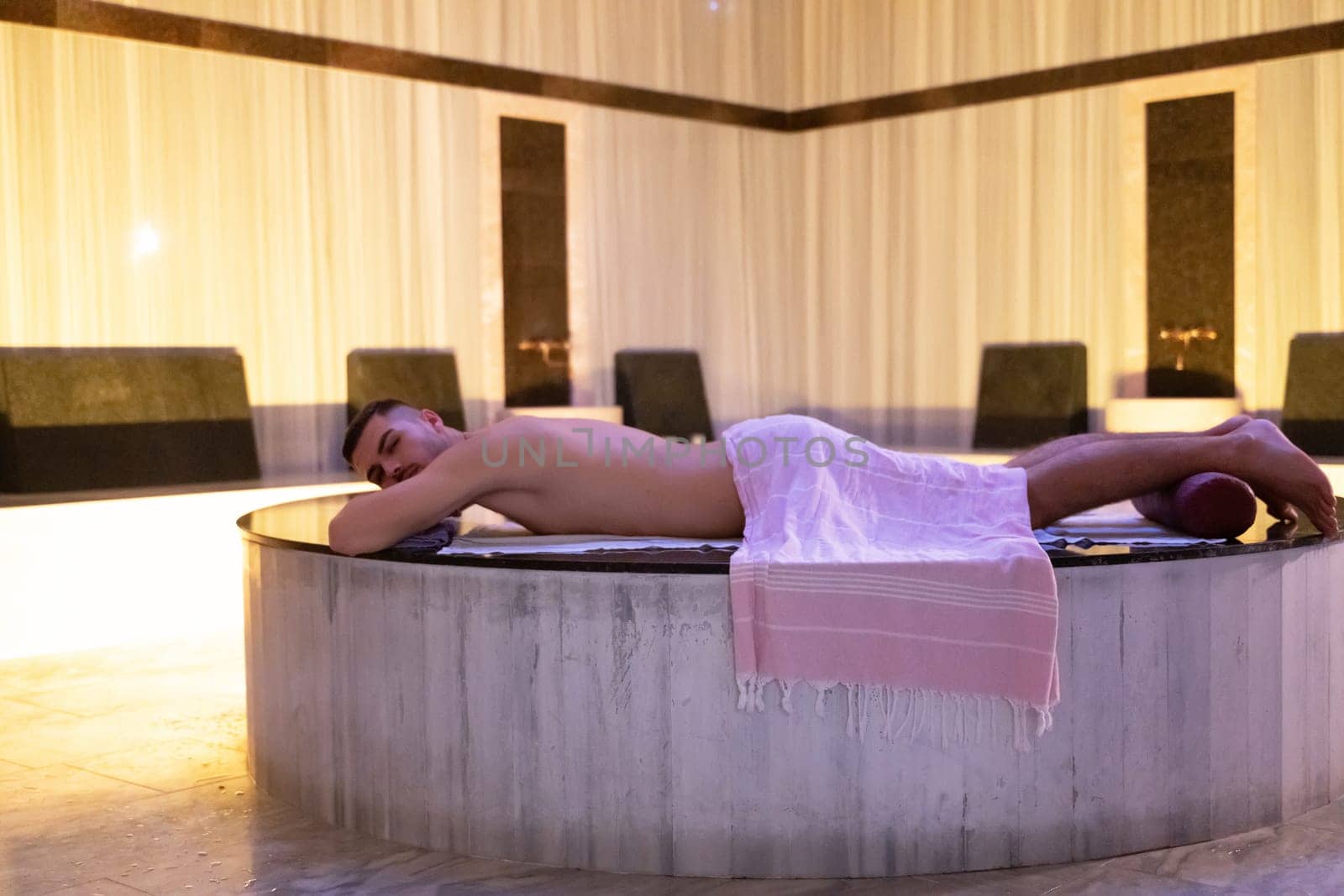 Turkish Bath Relaxation.Man relaxing on a marble platform inside a Turkish bath with warm lighting.