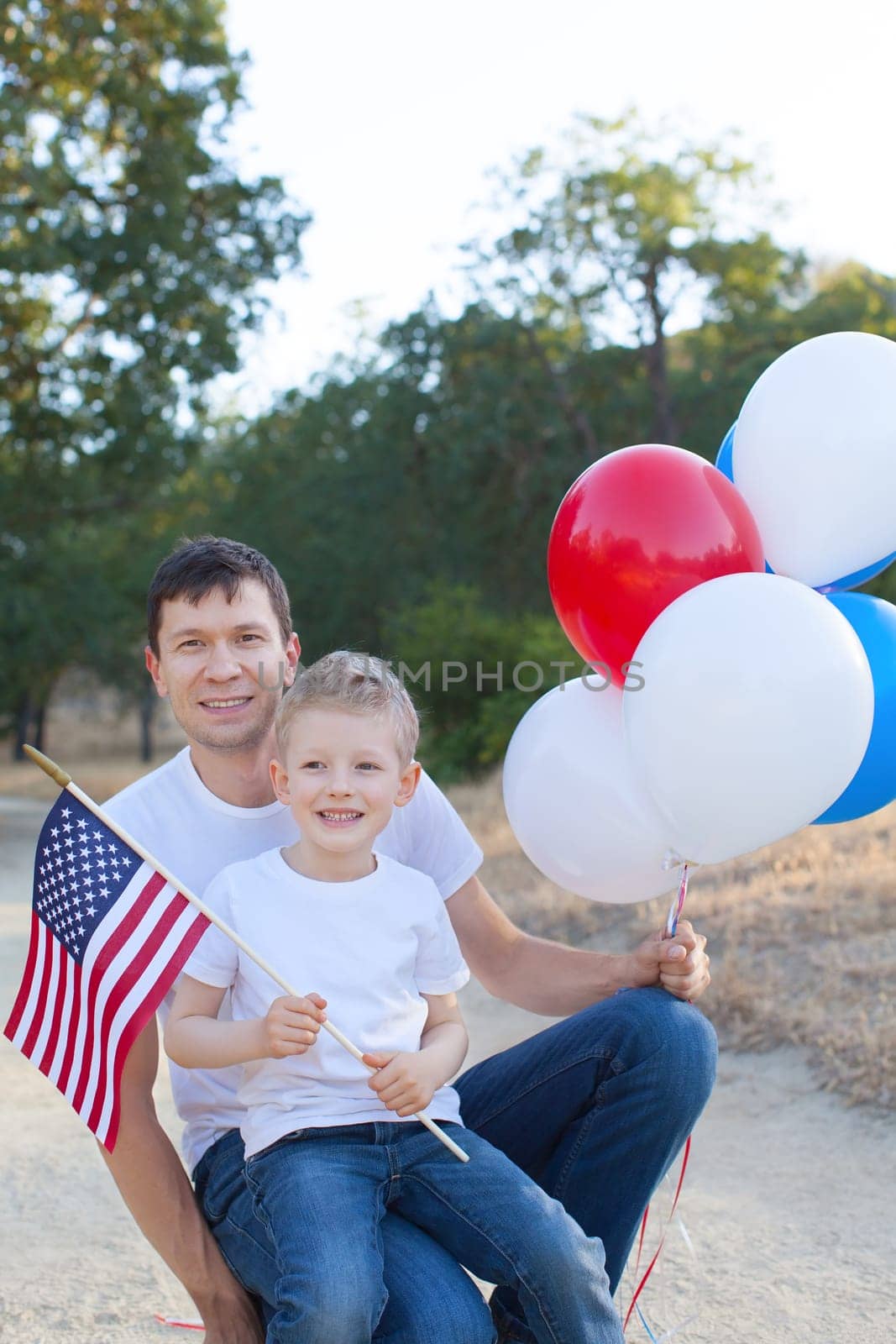 handsome father holding colorful balloons and his little son holding american flag celebrating 4th of July