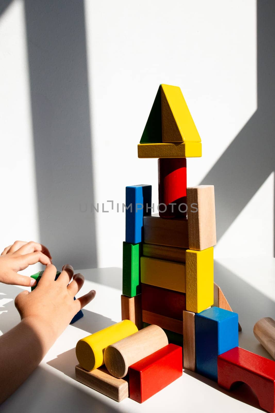 Child playing with colorful wooden building blocks in sunlit room. High quality.