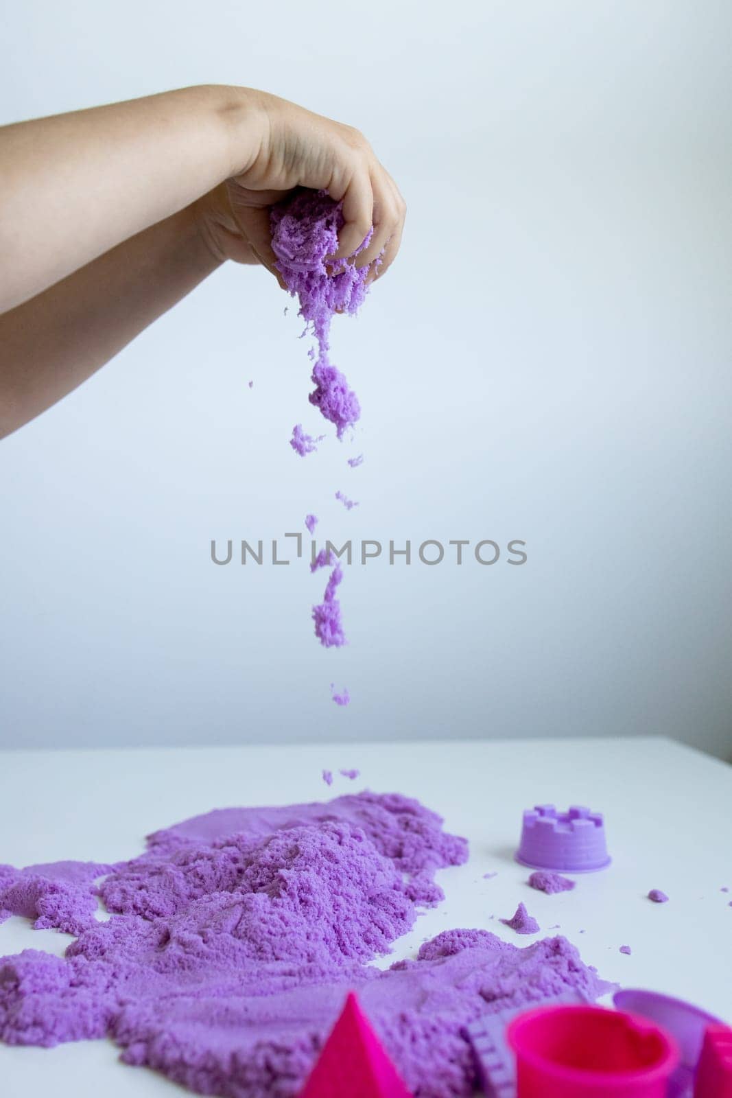 Child playing with purple kinetic sand on white surface. High quality.