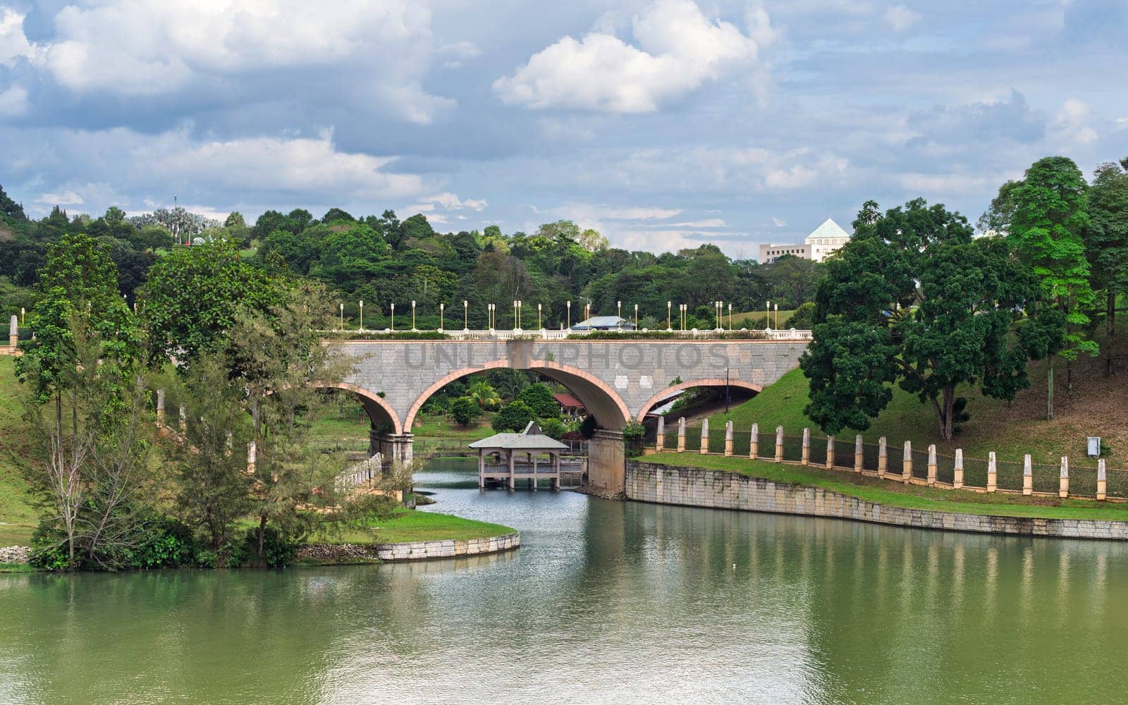 Bridge over Putrajaya lake, Putrajaya, Kuala Lumpur, Malaysia. Lush park scenery under cloudy sky