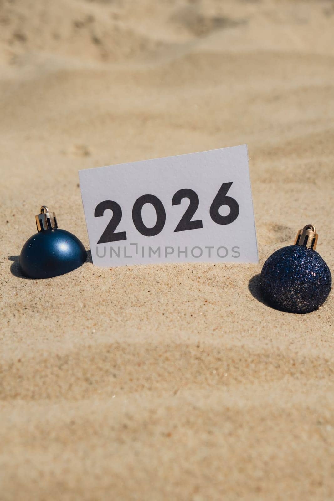 2026 text on paper greeting card on background sandy beach sun coast. Christmas balls New Year New Me decoration. Summer vacation decor. Holiday concept calendar date postcard. Getting away Travel Business concept