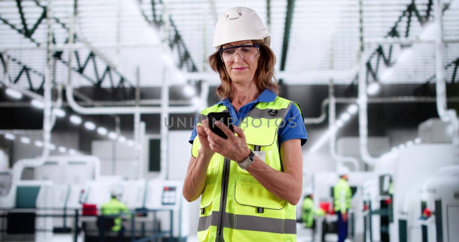 Female Factory Worker Inspecting Automated Production Line While Using Smartphone.