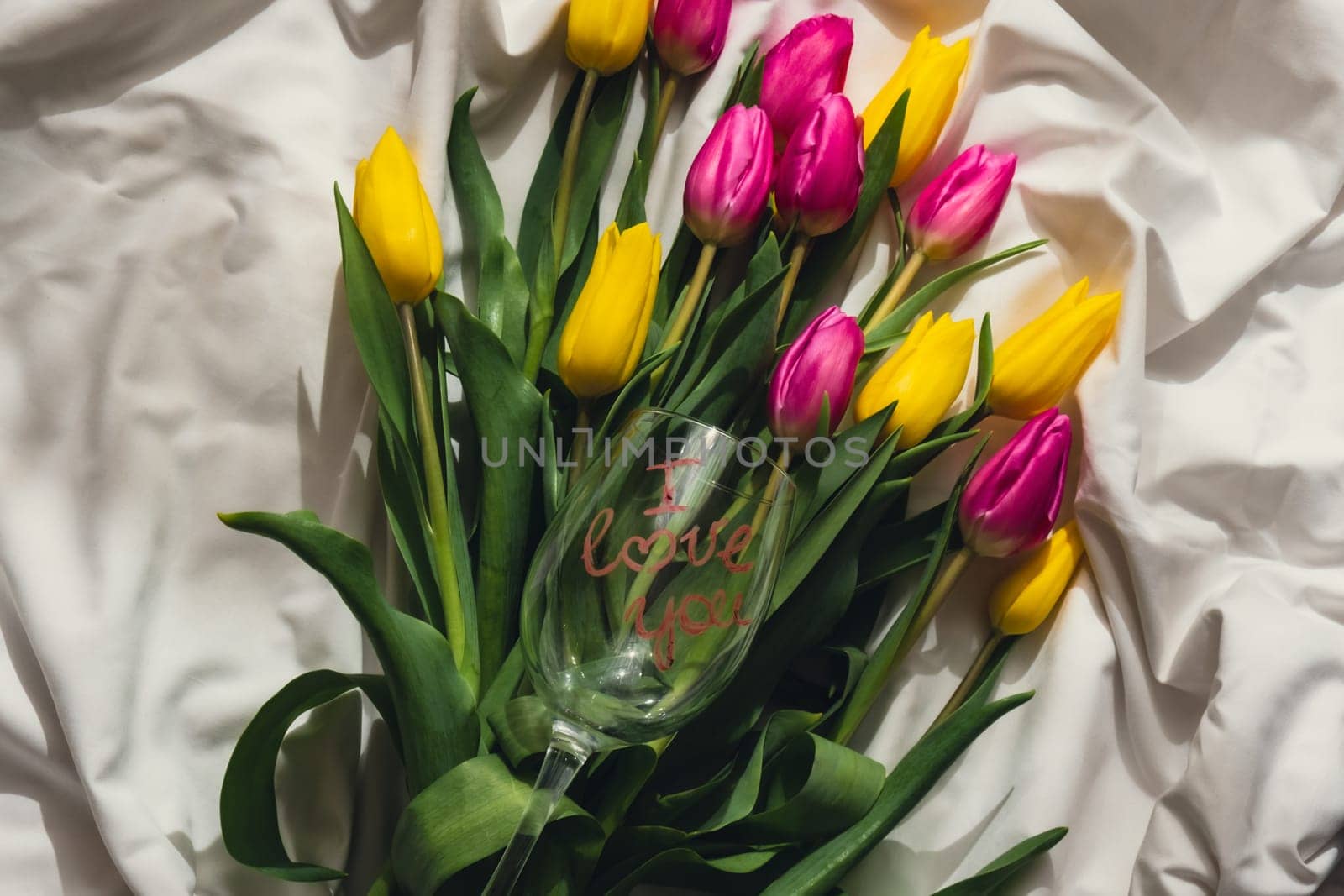 Wine glass with words I LOVE YOU Fresh bouquet of colorful tulip flowers on bed. Gift present idea for holiday birthday 8 March Mother's Day Valentine's day Women's Day. Copy space
