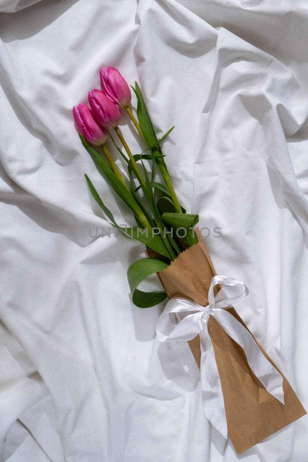 Bouquet of pink tulips in craft eco-friendly paper bag on messy bed. Romantic morning scene. Greeting card Holiday flowers springtime atmosphere