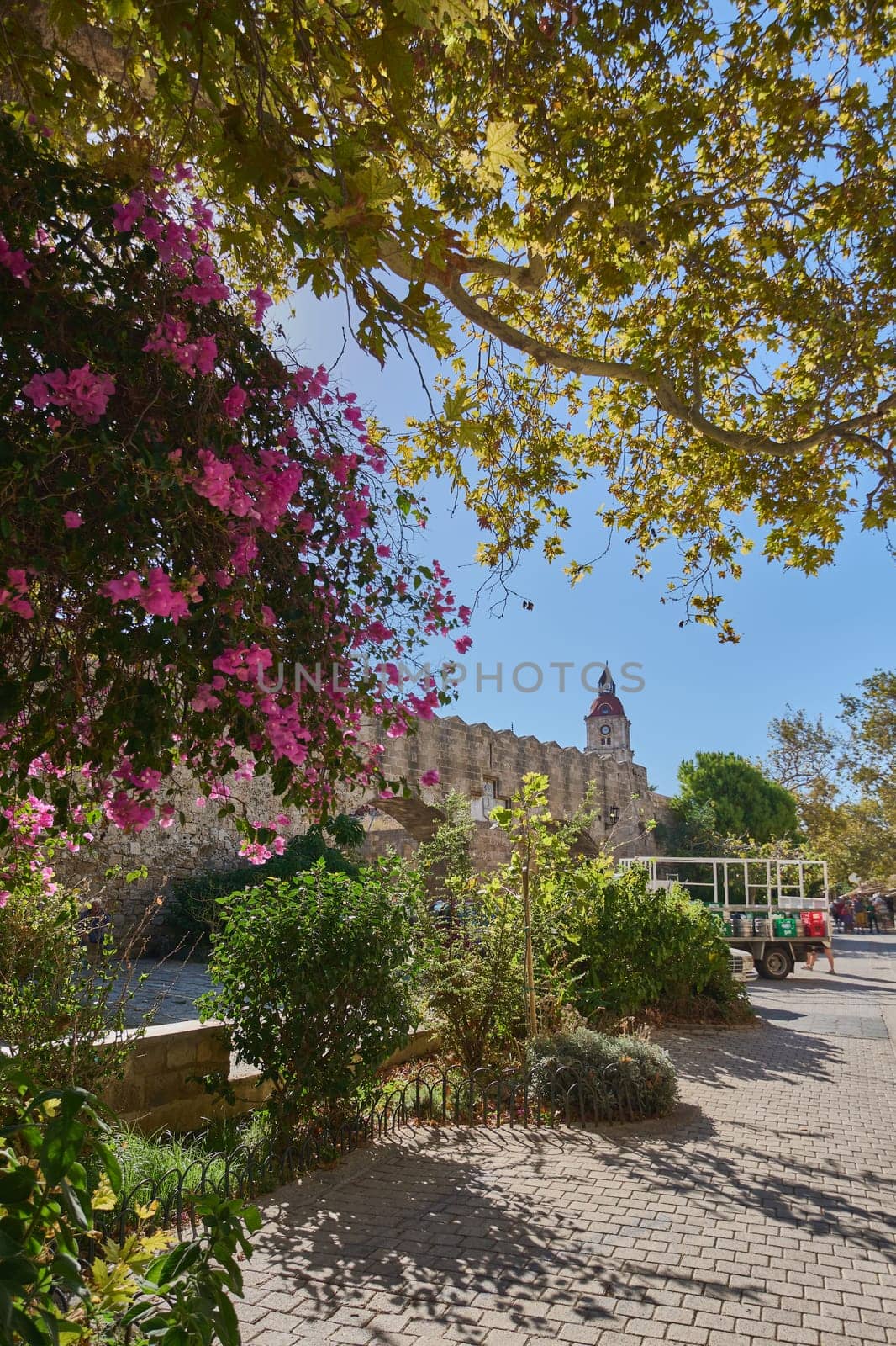 Rodas.Greece - june 01, 2025: Historical city, featuring a pathway alongside a medieval wall adorned with colorful flowers, leading to the renowned Palace of the Grand Masters.
