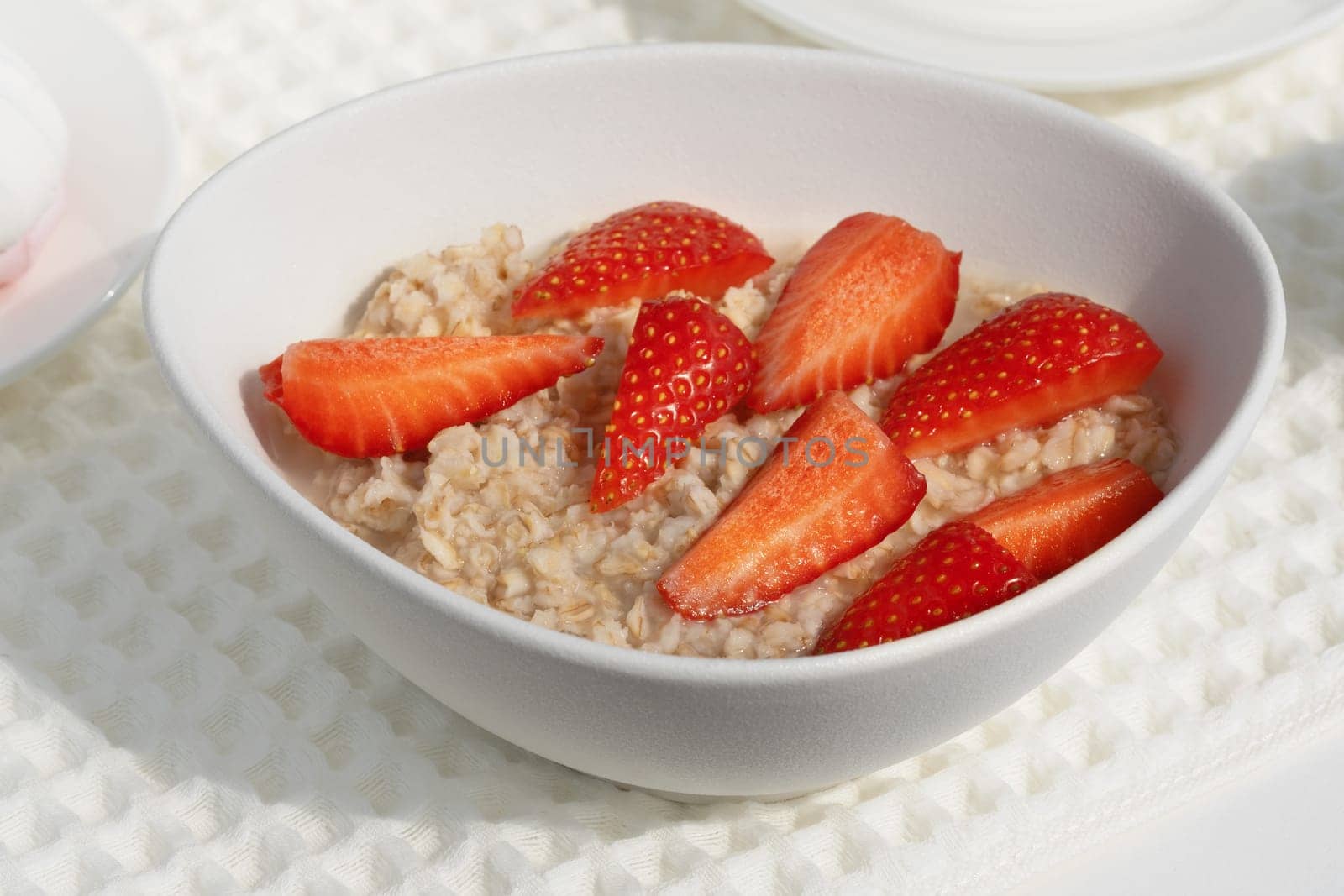 A bowl of creamy oatmeal is garnished with vibrant, sliced strawberries, creating a colorful breakfast dish. The setting is bright and cheerful, ideal for a healthy start.
