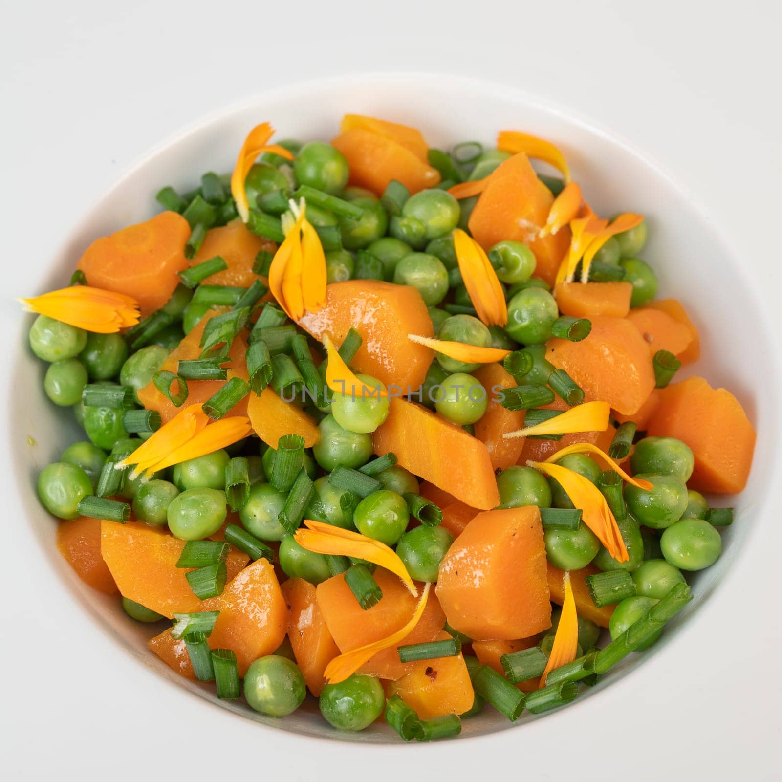 Fresh garden peas and carrots are cooked with salted butter, then garnished with chives and bright marigold flowers for an appealing and colorful side dish.