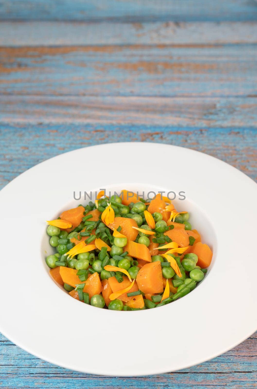 Fresh garden peas and carrots are cooked with salted butter, then garnished with chives and bright marigold flowers for an appealing and colorful side dish.