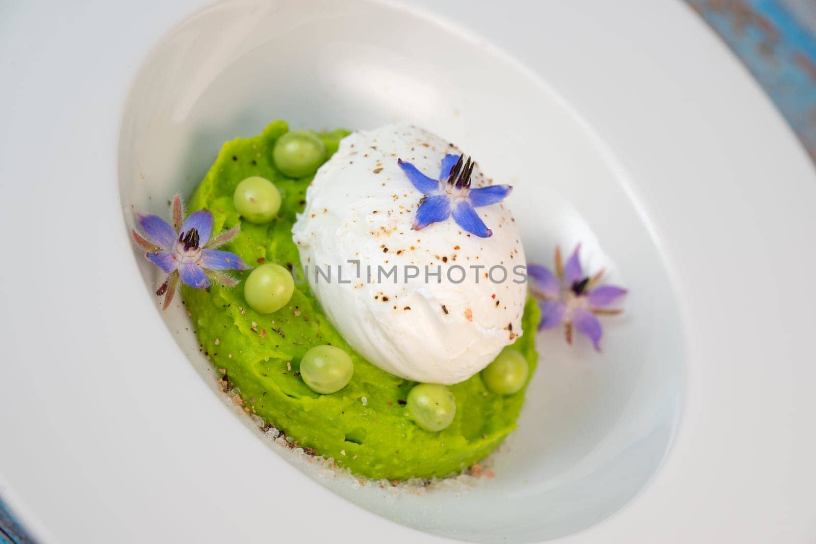 A fresh pea puree is beautifully plated, featuring a poached egg at the center and adorned with borage flowers. The dish showcases vibrant colors and textures, perfect for any spring menu.
