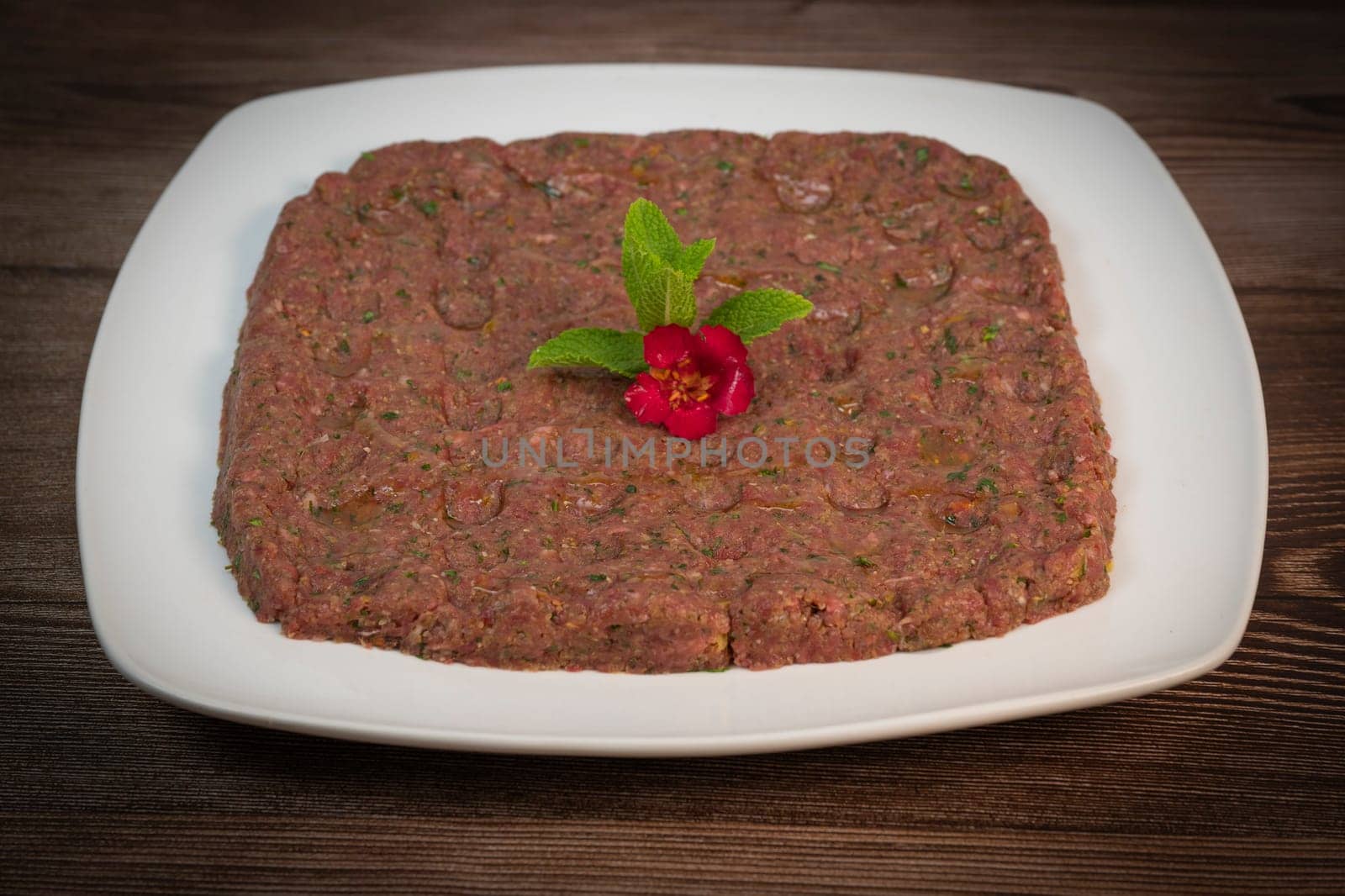 Kebbe naye is showcased on a white plate, featuring finely chopped raw meat mixed with bulgur, onions, mint, and spices, designed for a rich culinary experience.