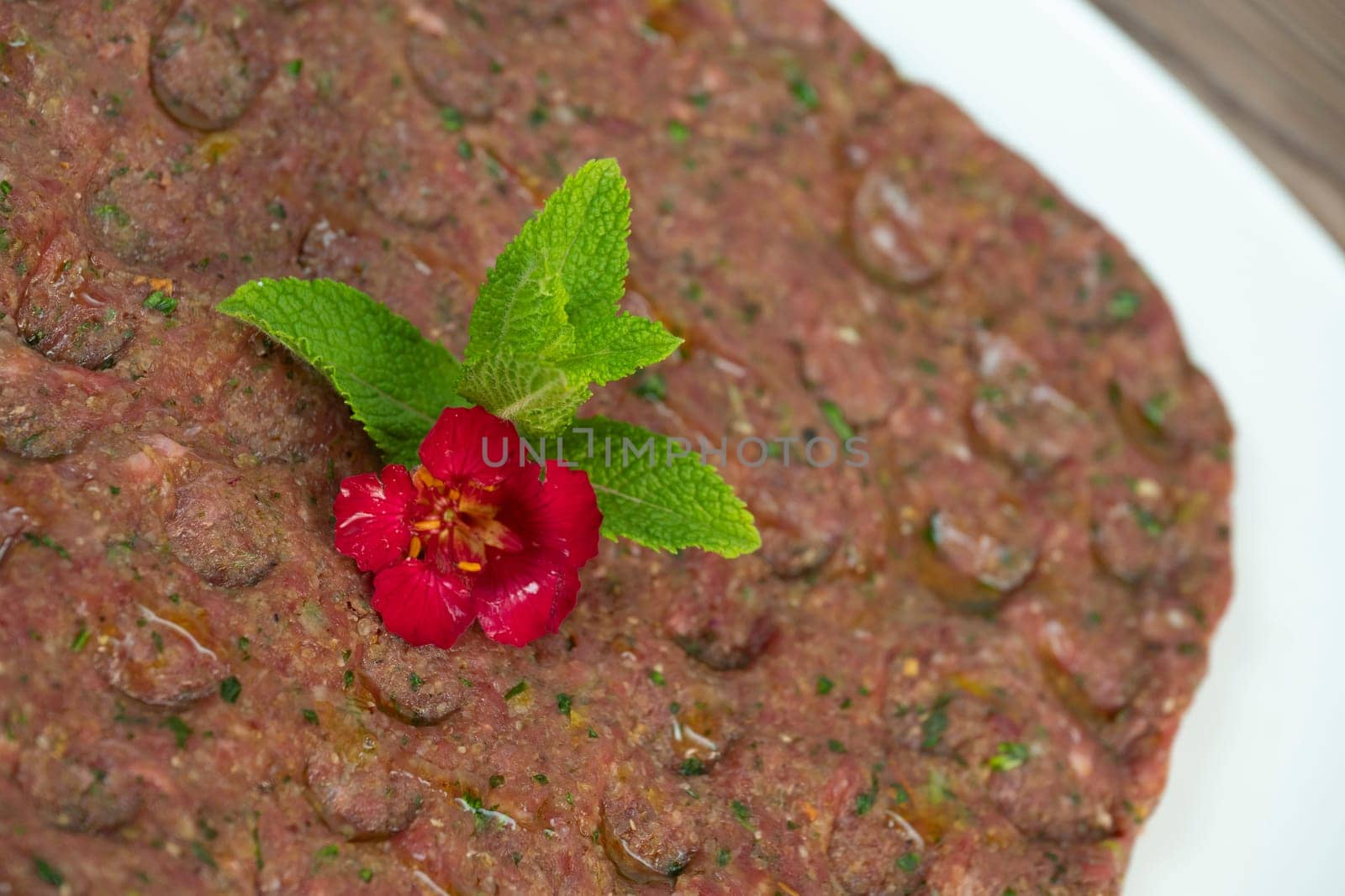 Kebbe naye is showcased on a white plate, featuring finely chopped raw meat mixed with bulgur, onions, mint, and spices, designed for a rich culinary experience.