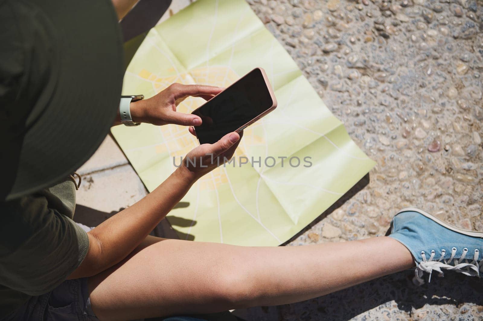 An individual examines their smartphone while sitting near an unfolded map of a historic city. The image captures a traveling moment filled with adventure and outdoor exploration.