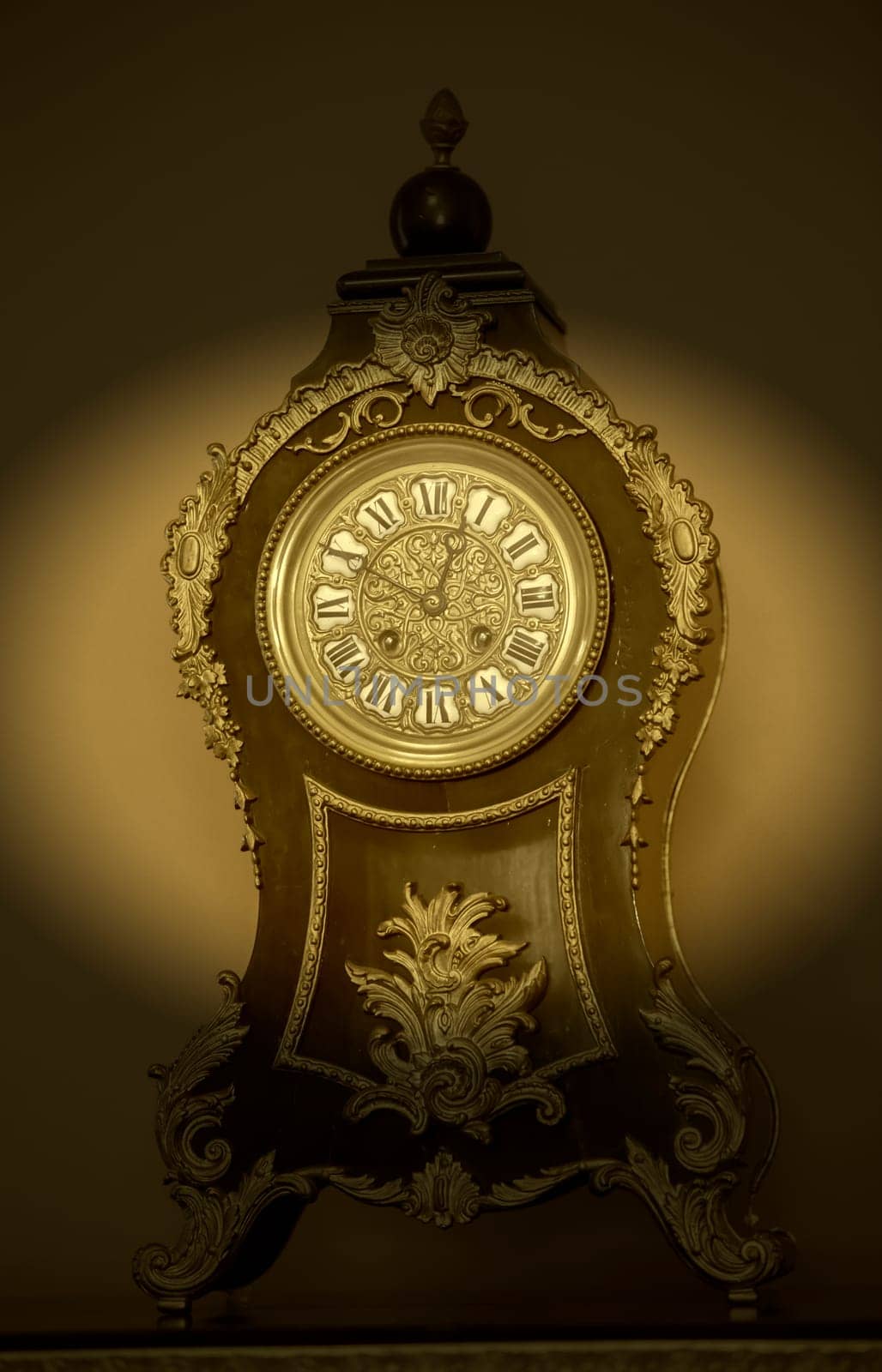 Vintage wooden table clock with nineteenth century golden elements in dark vignette.