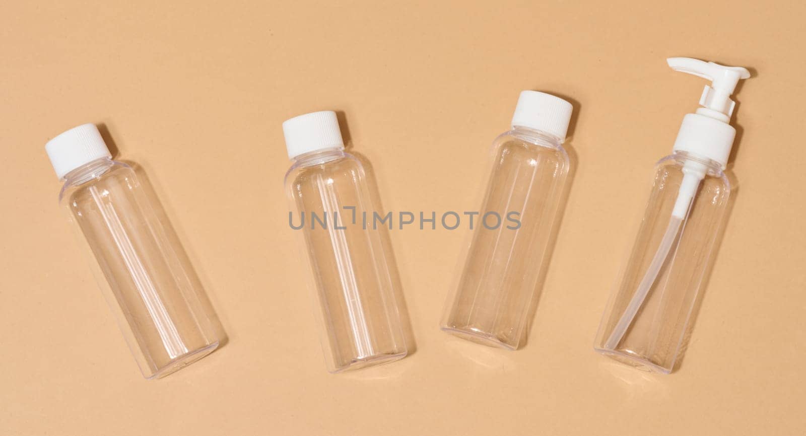 Travel set of plastic bottles for cosmetics on beige background, top view