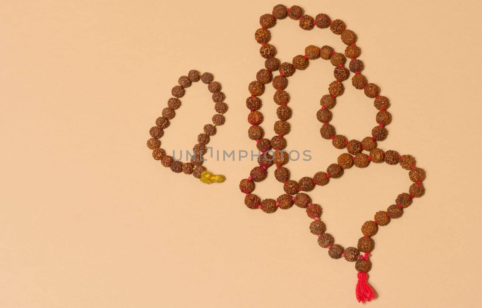 Top view of two strands of rudraksha beads, one of which is longer and has a red tassel, placed on a beige background