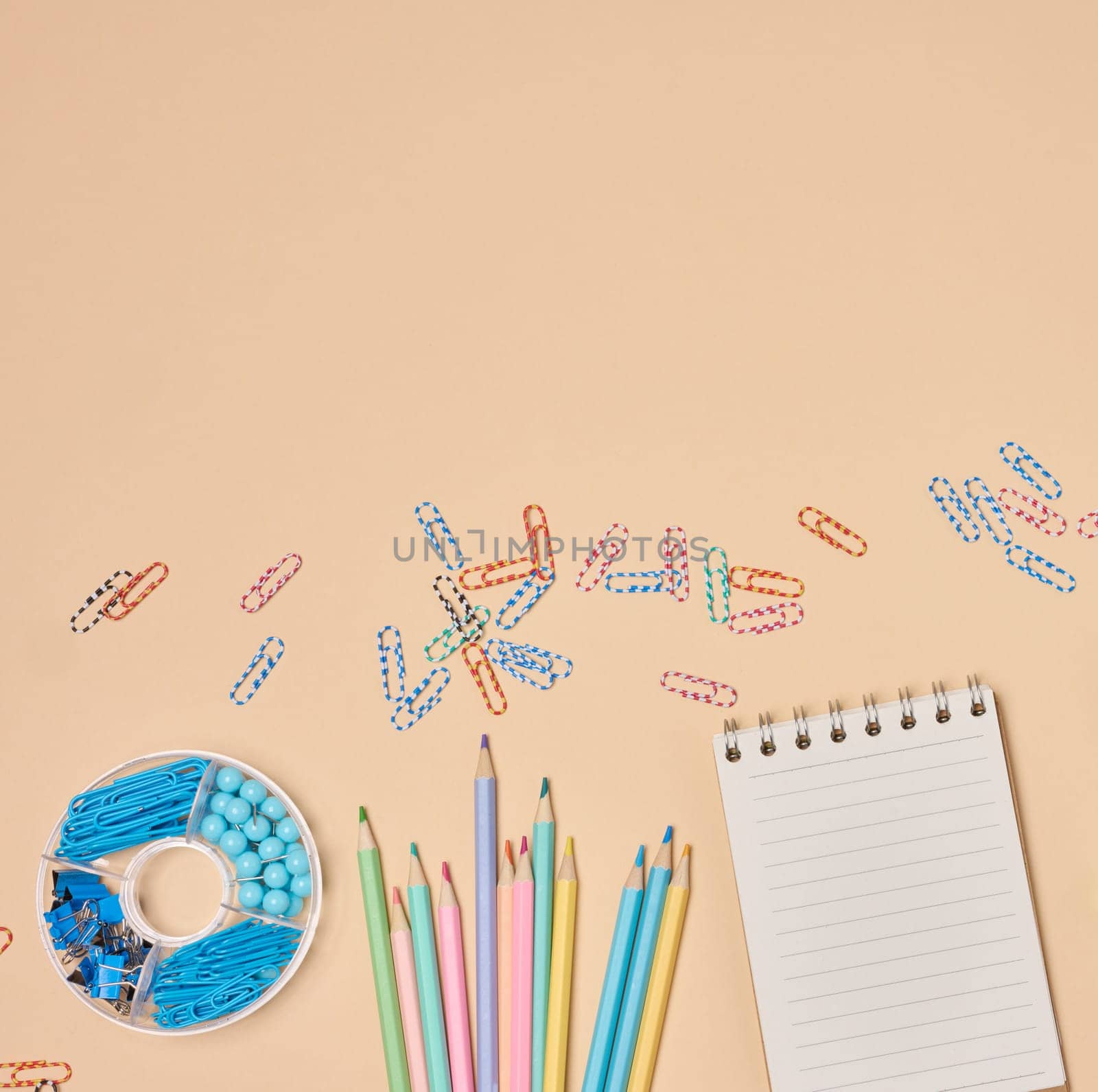 Flat lay of colorful school and office supplies including pencils, paper clips, notebooks on a peach background. Creative workspace concept.