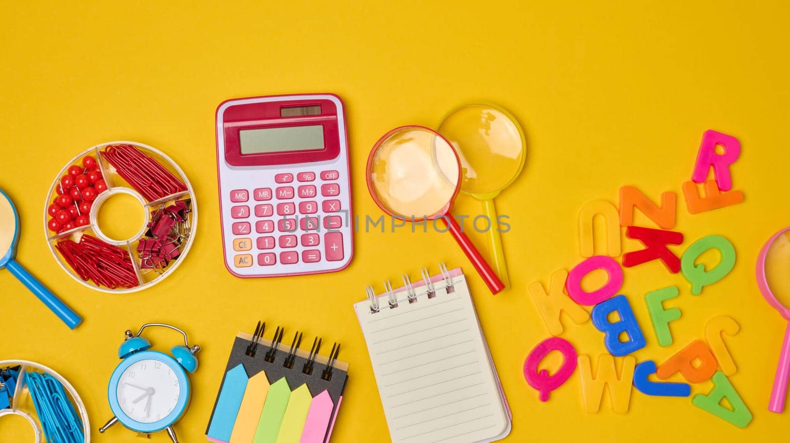 Vibrant collection of colorful school supplies, building bricks, letters, and learning items scattered on a yellow background. Play and education concept.