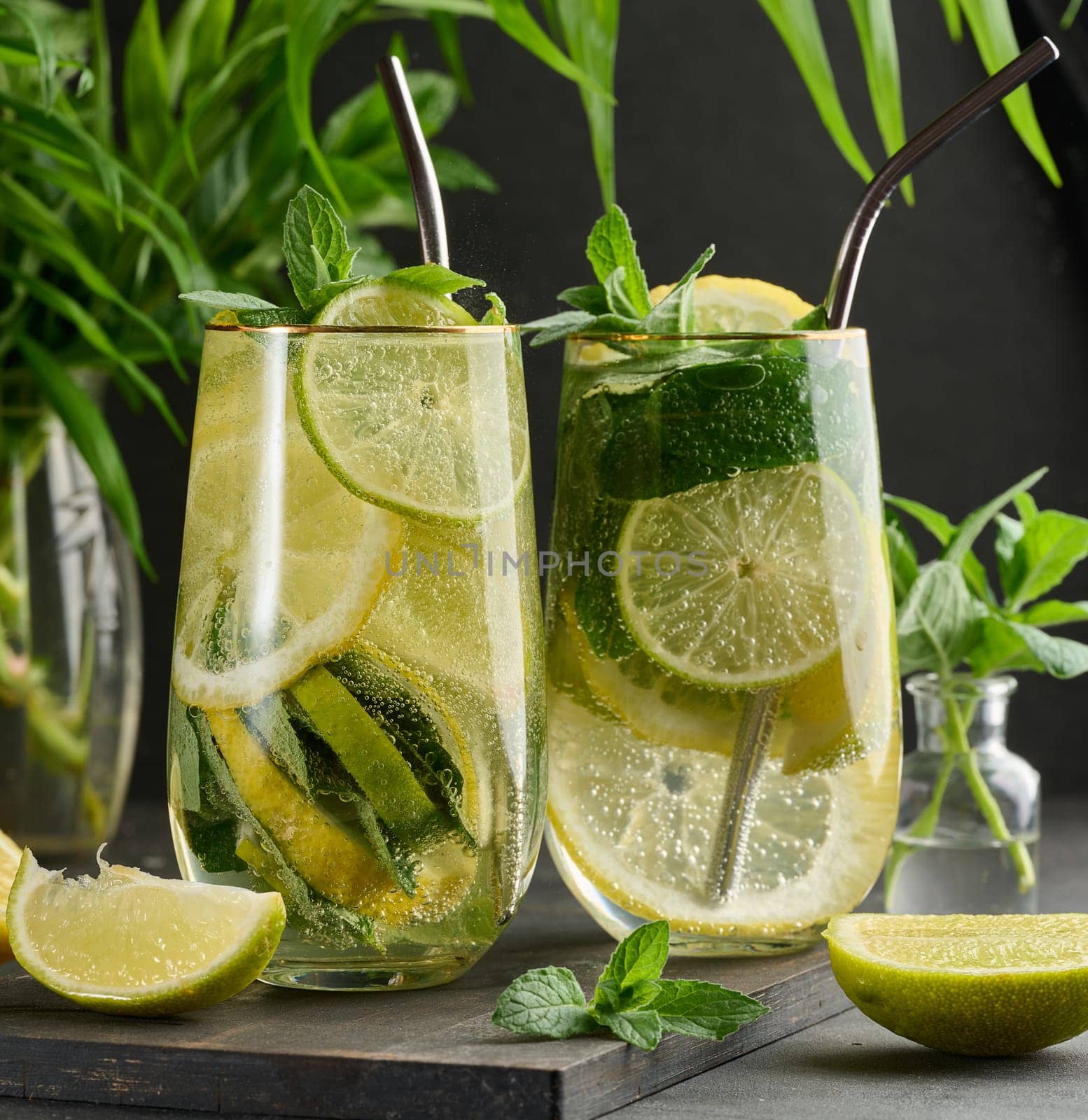 Refreshing detox or summer drink in a glass with lemon, lime, mint, ice, and metal straw. Dark background