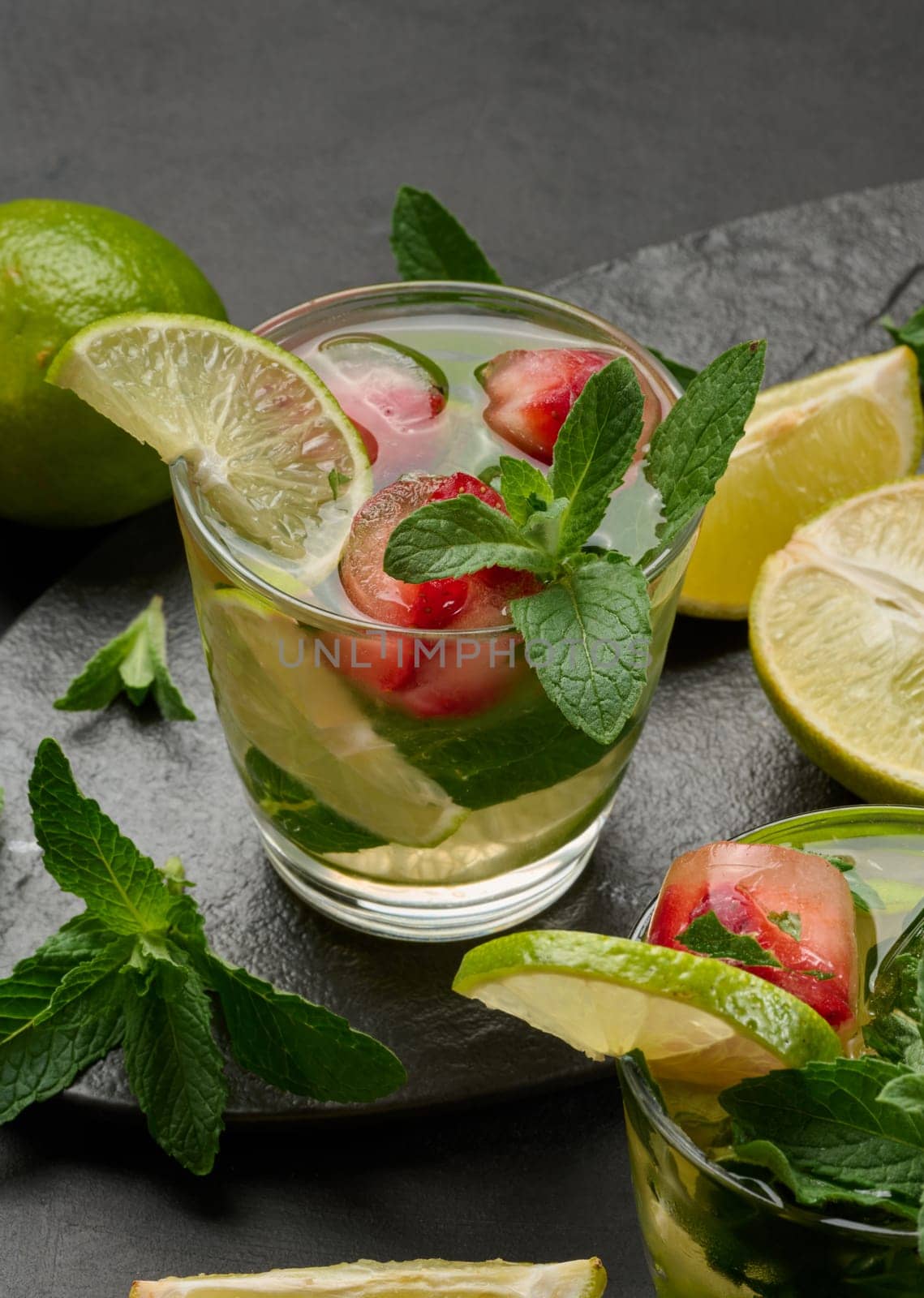 Refreshing mojito cocktail with lime, mint, strawberry, and ice on dark background, top view