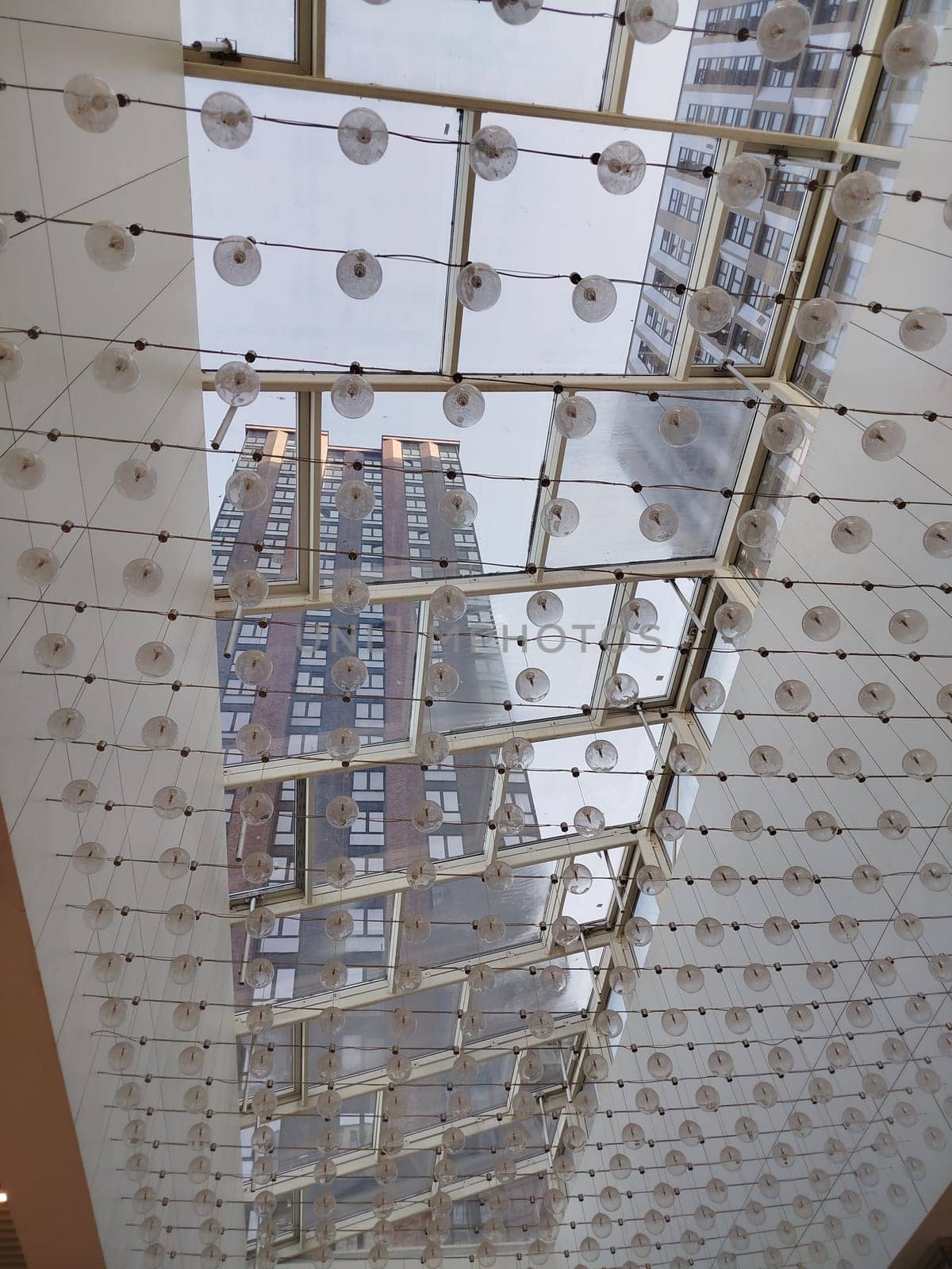 Looking up at apartment buildings through a glass roof with suspended decorations. The roof has a grid pattern. The time of day seems to be daytime.