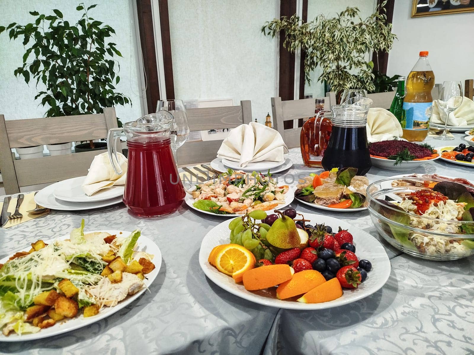 A table is laden with various salads, fruit plates, and drinks. A white tablecloth provides the backdrop for the diverse dishes at this festive meal, likely in a restaurant.