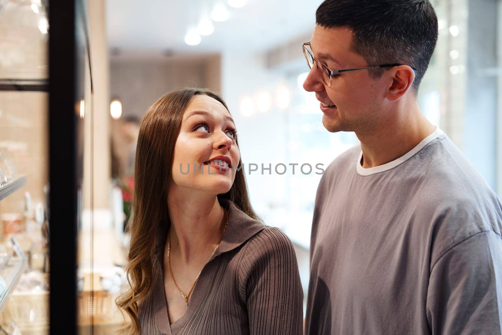 Two people share a joyful moment in a bright cafe. They gaze at each other while looking at a tempting array of desserts. The ambiance is cozy and inviting.