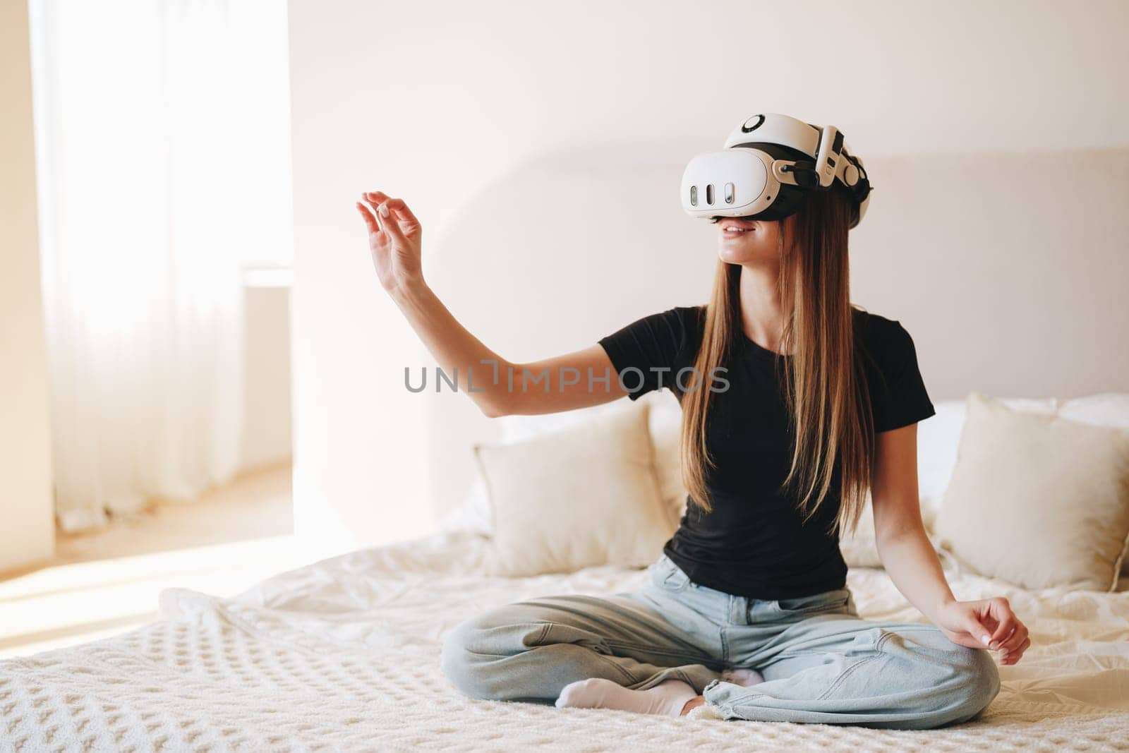 A young woman sits cross-legged on a bed, fully engaged in a virtual reality activity. Sunlight fills the room, creating a relaxing atmosphere as she interacts with digital content.