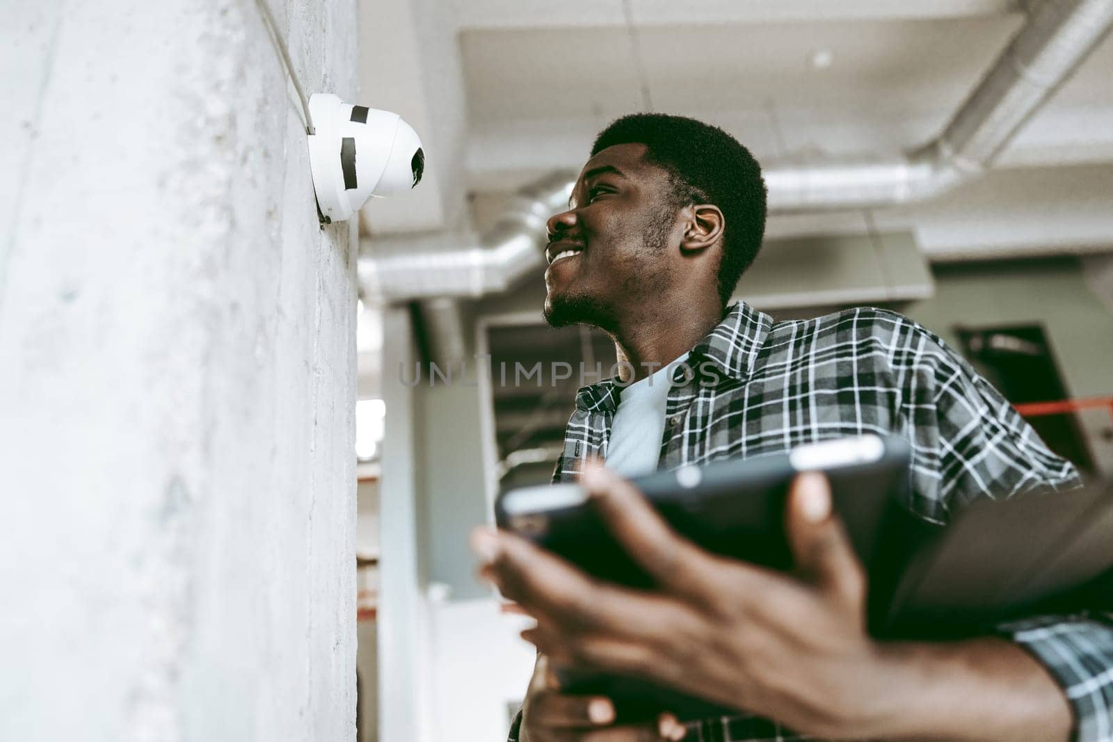 A young man, smiling and dressed casually, interacts with an innovative device mounted on a wall in a bright, modern office setting during the afternoon.