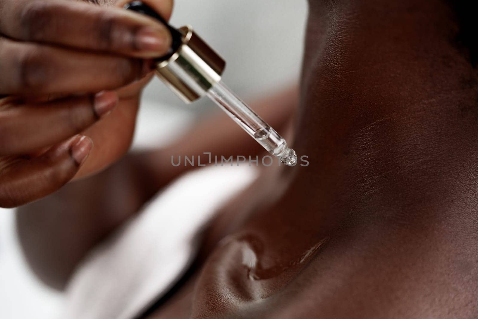 A person carefully applies a dropper of facial serum to their neck, showcasing the detailed skincare routine in a serene treatment space. Relaxation and self-care are evident.