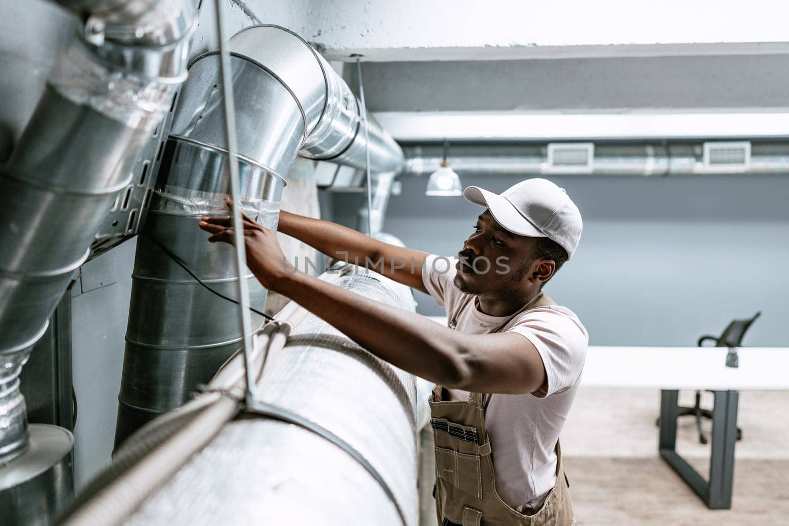 A technician carefully examines the ventilation ducts in a contemporary office setting. Wearing work attire, he ensures proper function and safety of the air system.