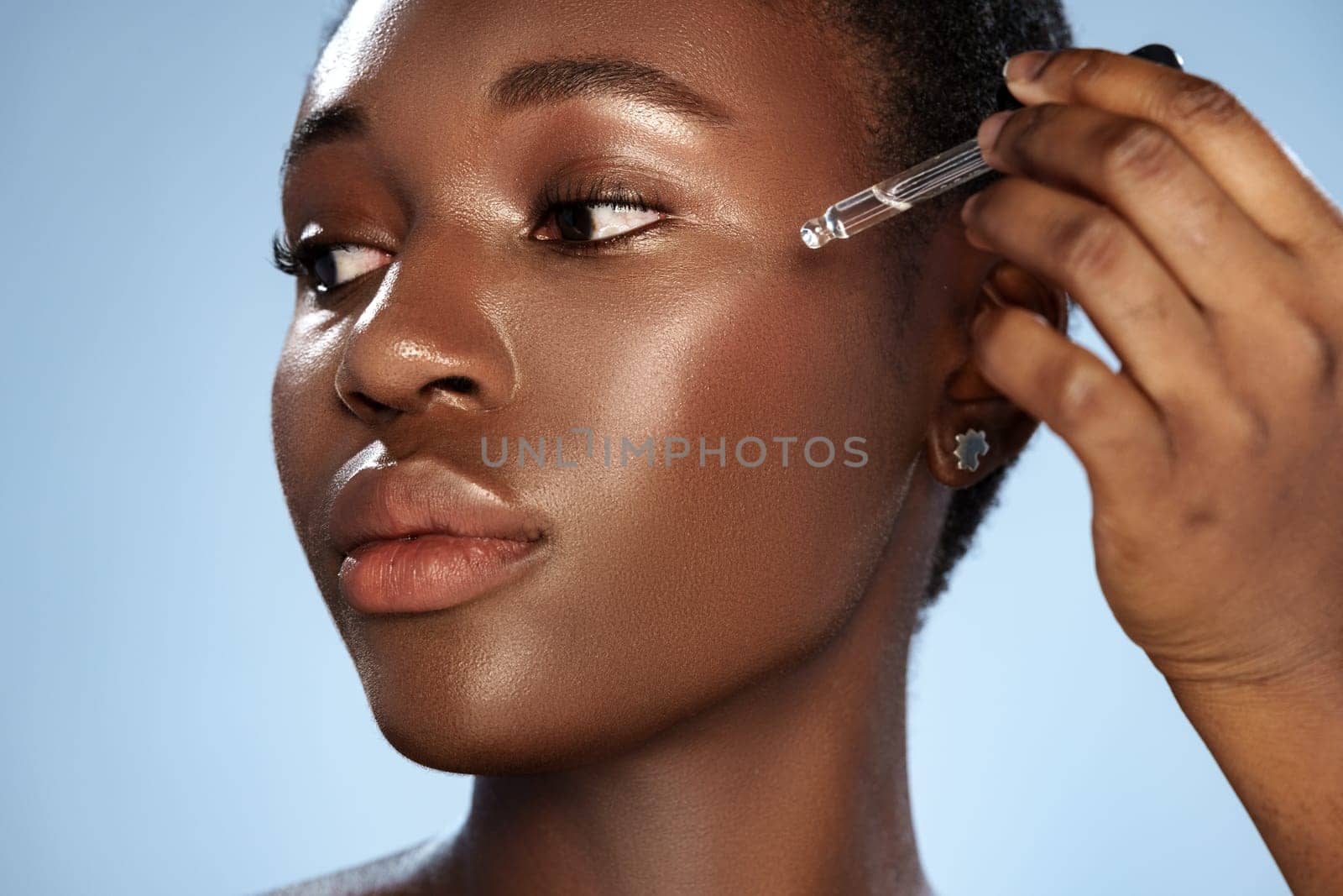 A woman focuses on applying a serum to her cheek in a well-lit area, highlighting her glowing skin. The serene background complements her beauty routine.